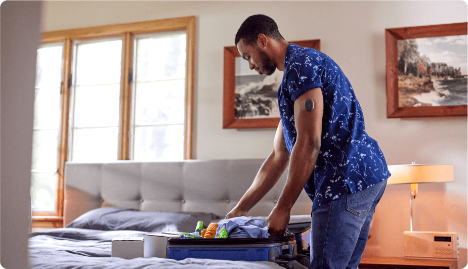 Eversense Benutzer packt Kleidung in einen Koffer auf einem Bett, in einem gem&uuml;tlichen Schlafzimmer mit gerahmten Bildern und Fenstern.