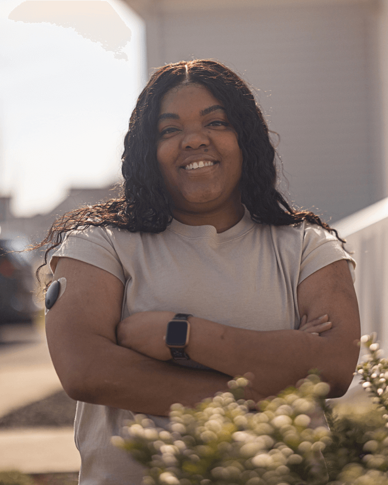 Mary, eine Eversense Benutzerin seit 2020, steht im Freien mit ihrem CGM Transmitter am Arm.