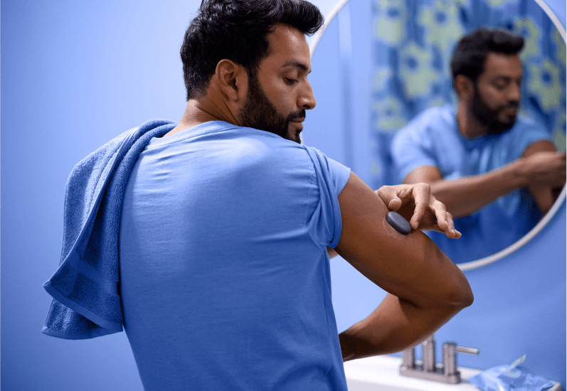 Eversense Benutzer nimmt das einfach abnehmbare CGM Gerät vor einem Spiegel ab.